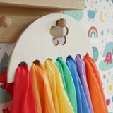 Close up of Laura's Play Cotton large Wooden Display holder with flower cut out decoration hung up with 7 play cloths inside.