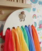 Close up of Laura's Play Cotton large Wooden Display holder with flower cut out decoration hung up with 7 play cloths inside.