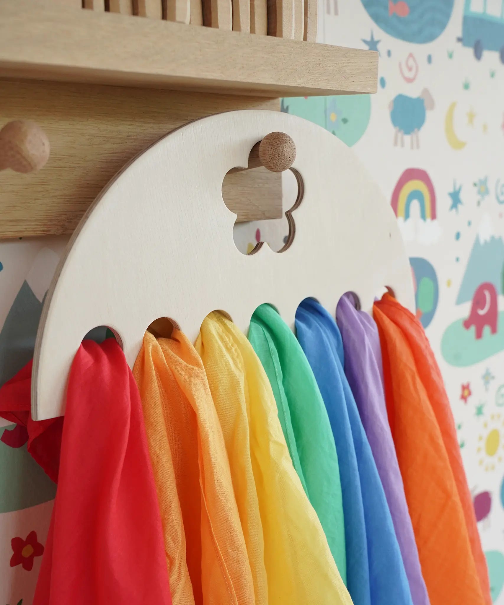 Close up of Laura's Play Cotton large Wooden Display holder with flower cut out decoration hung up with 7 play cloths inside.