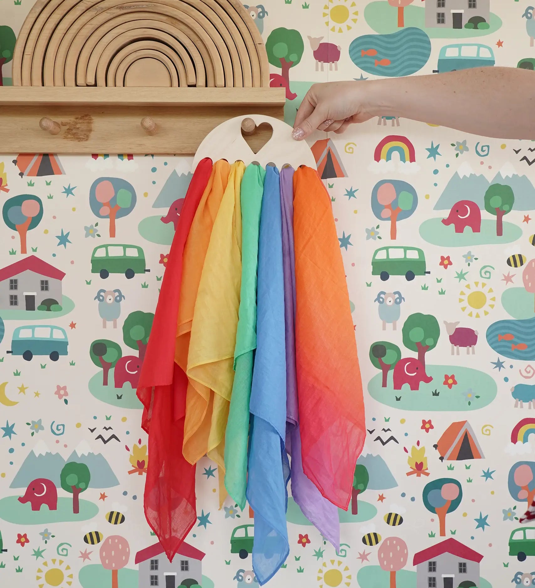 Laura's Play Cotton large Wooden Display holder with heart cut out with 7 play cloths inside placed on a peg shelf.