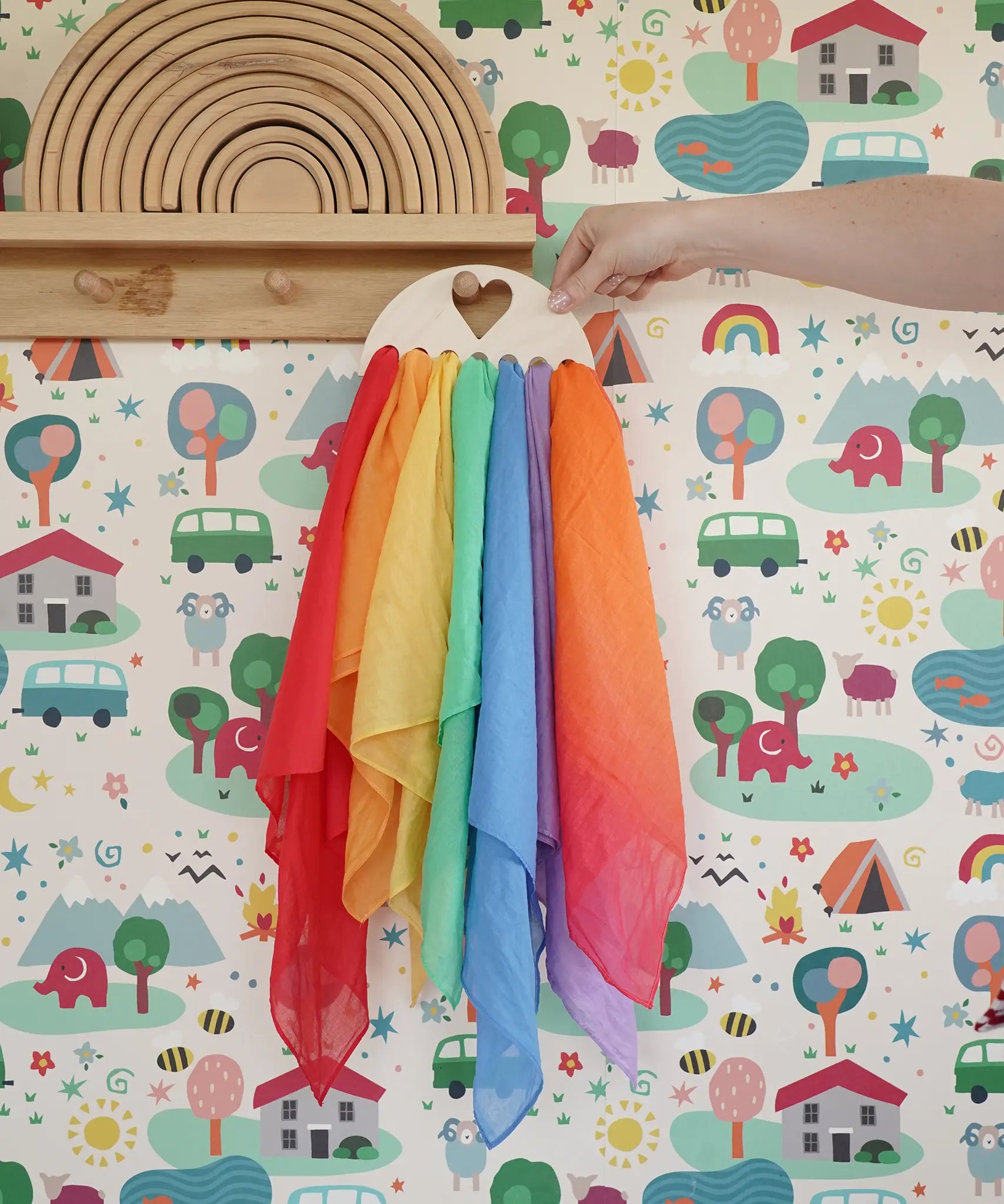 Laura's Play Cotton large Wooden Display holder with heart cut out with 7 play cloths inside placed on a peg shelf.