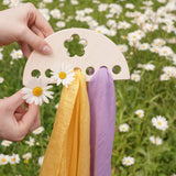 Laura's Play Cotton small Wooden Display holder with flower cut out decoration in an adult's hand with two cloths placed on it and some daisies. 
