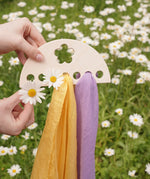 Laura's Play Cotton small Wooden Display holder with flower cut out decoration in an adult's hand with two cloths placed on it and some daisies. 
