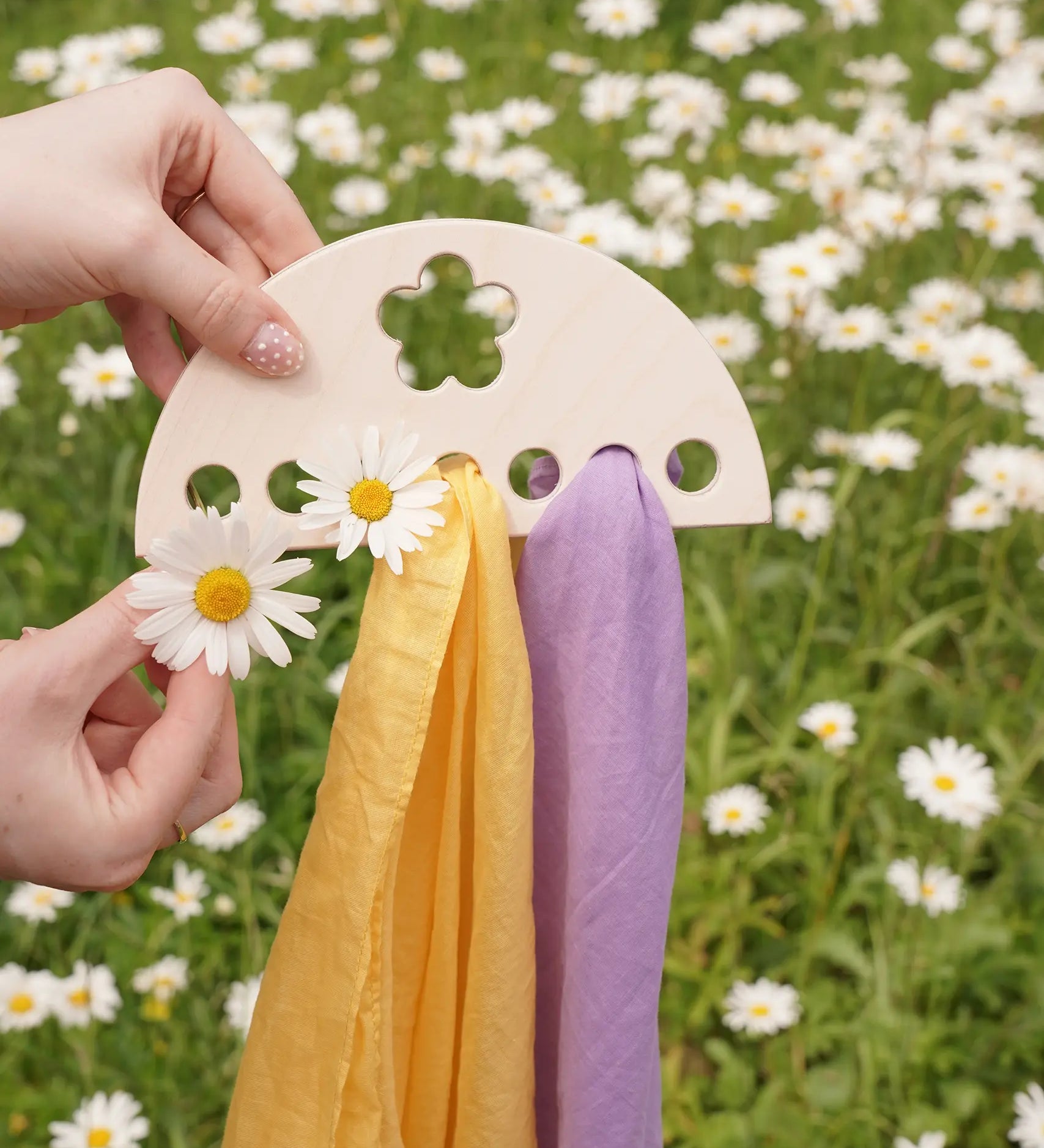 Laura's Play Cotton small Wooden Display holder with flower cut out decoration in an adult's hand with two cloths placed on it and some daisies. 
