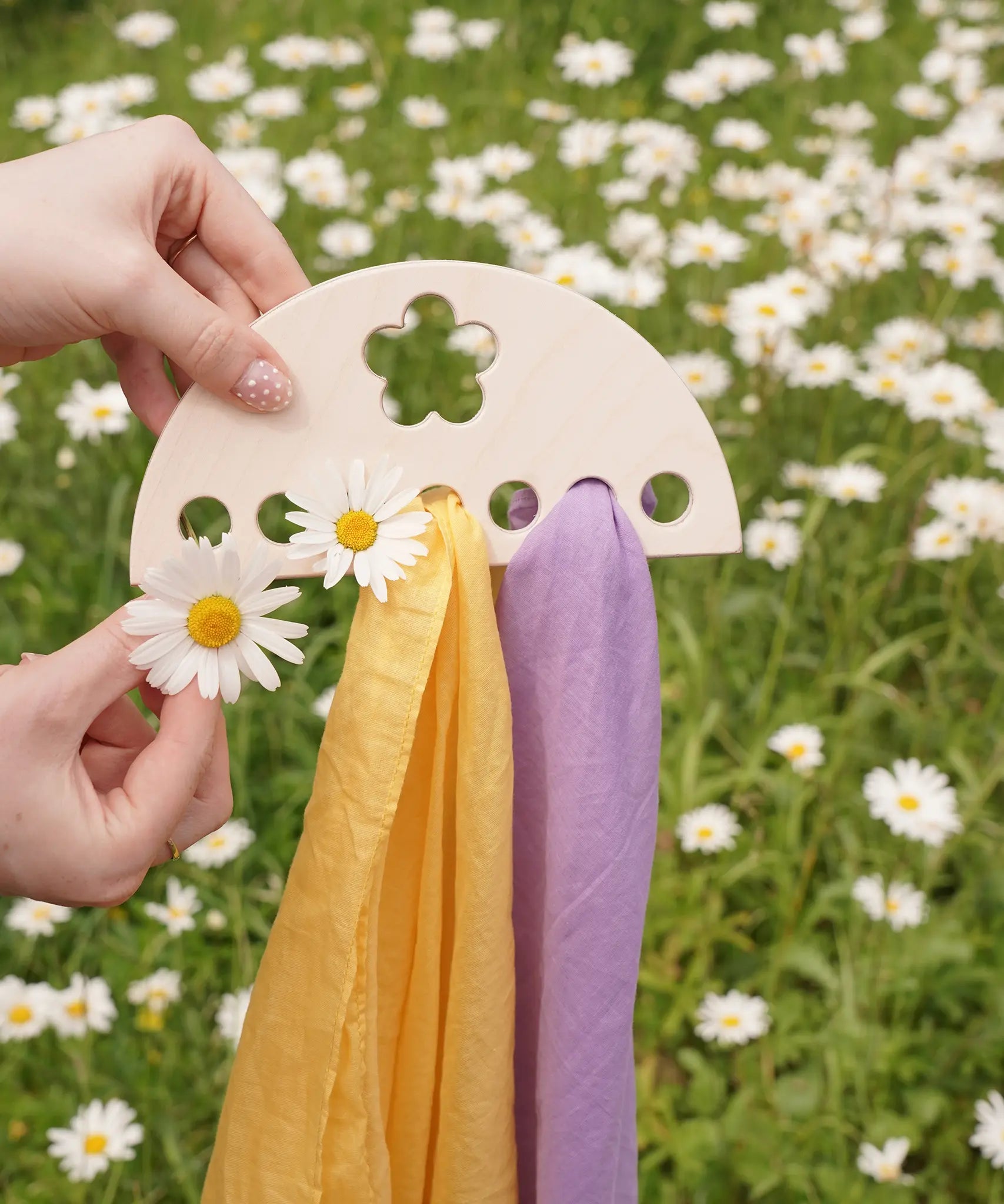 Laura's Play Cotton small Wooden Display holder with flower cut out decoration in an adult's hand with two cloths placed on it and some daisies. 