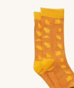 A close up of the Little Green Radicals golden leaves ankle showing the yellow autumn inspired  leaves design on orange organic cotton fabric with yellow trim.