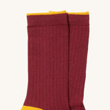 A close up of the maroon Little Green Radicals ankle sock. Showing the soft ribbed stitch and yellow trim on organic cotton fabric.