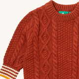 A close up of the Little Green Radicals ginger aran knitted jumper available at Babipur. Showing the cable knit and the thick collar detail on dark orange organic cotton fabric