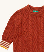 A close up of the Little Green Radicals ginger aran knitted jumper available at Babipur. Showing the cable knit and the thick collar detail on dark orange organic cotton fabric