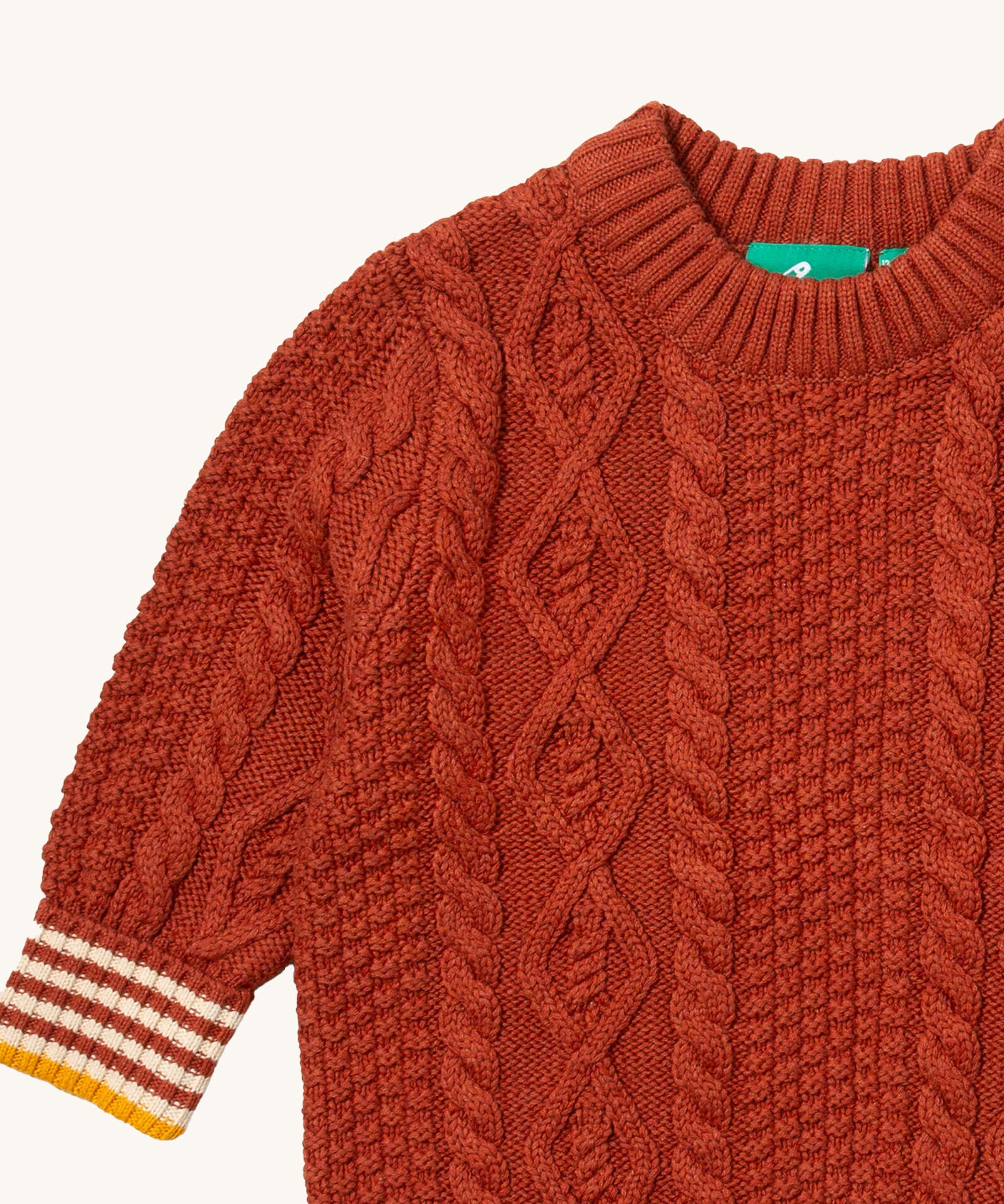 A close up of the Little Green Radicals ginger aran knitted jumper available at Babipur. Showing the cable knit and the thick collar detail on dark orange organic cotton fabric