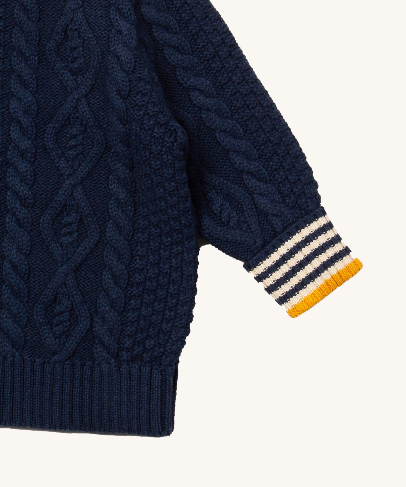 A close up of the Little Green Radicals navy aran knitted jumper available at Babipur. Showing the cable knit and the striped cuff detail on dark navy organic cotton fabric