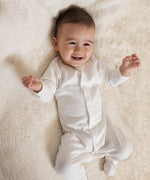 A baby lying down and wearing the Little Green Radicals footed babygrow showing the popper detail on white organic cotton fabric