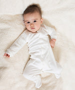 A baby lying down on a soft surfaceand wearing the Little Green Radicals footed babygrow showing the long sleeve and closed popper detail on white organic cotton fabric