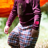 A close up of a child standing outside and wearing the dark maroon Little Green Radicals teddy bear applique long sleeve t shirt showing the apple applique detail. 
