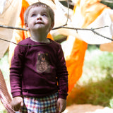 A child standing outside and wearing the dark maroon Little Green Radicals teddy bear applique long sleeve t shirt.