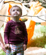 A child standing outside and wearing the dark maroon Little Green Radicals teddy bear applique long sleeve t shirt.