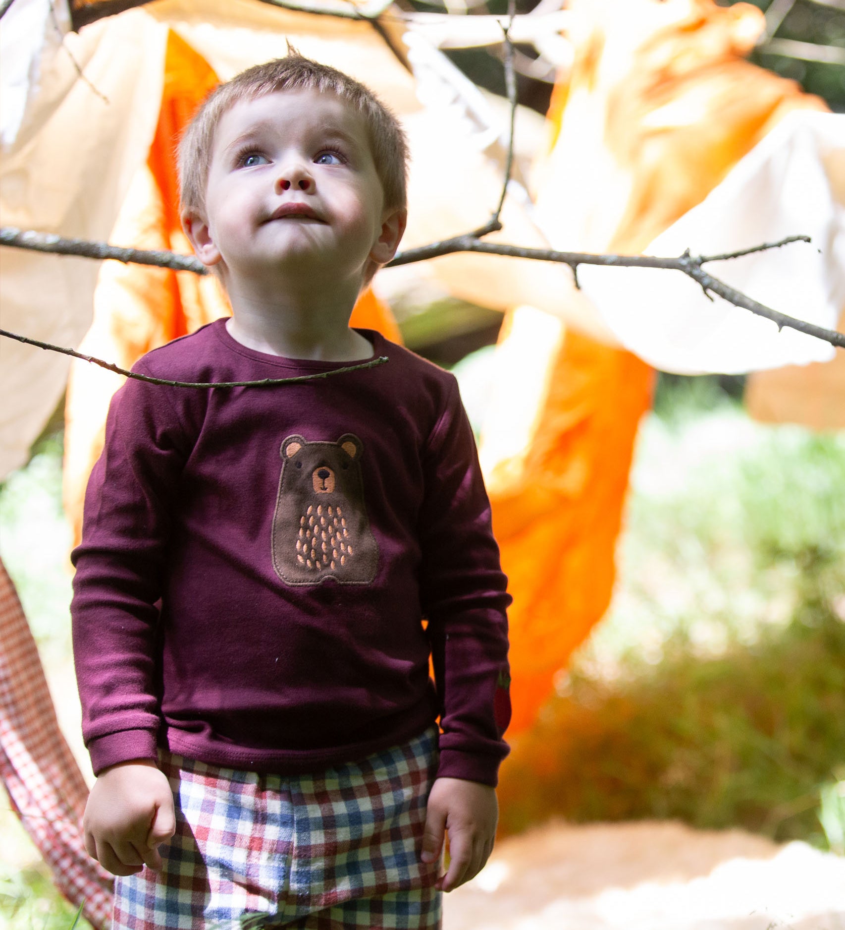 A child standing outside and wearing the dark maroon Little Green Radicals teddy bear applique long sleeve t shirt.