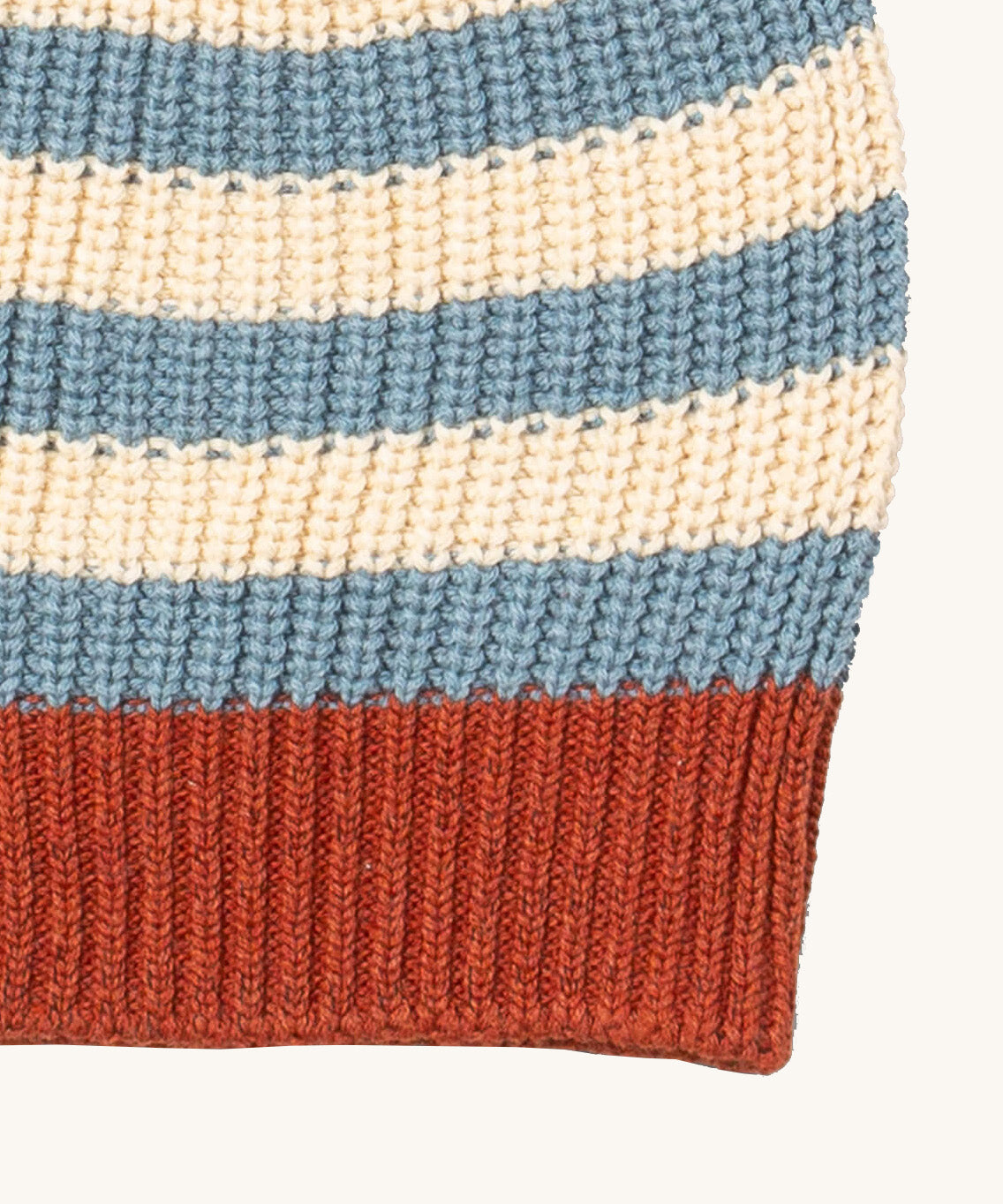A close up of the Little Green Radicals knitted beanie in blue stripes. Showing the thick red knit brim detail on organic cotton fabric