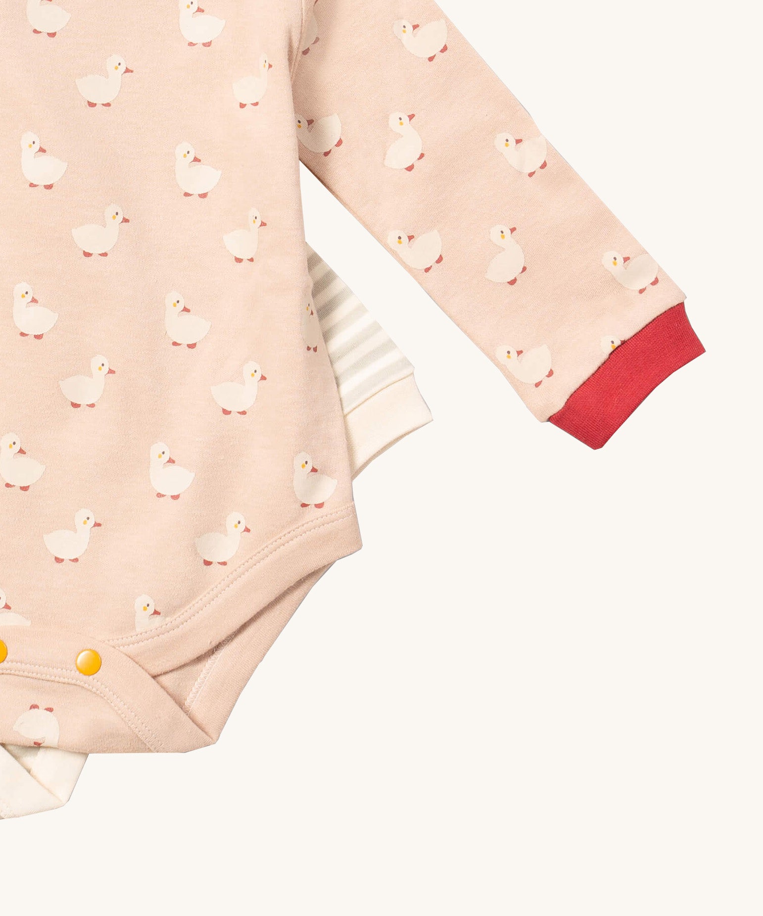 A close up of the puddle ducks Little Green Radicals baby body suit on top of the grey and cream striped bodysuit showing yellow popper detail around the crotch and leg hole detail on soft organic cotton fabric