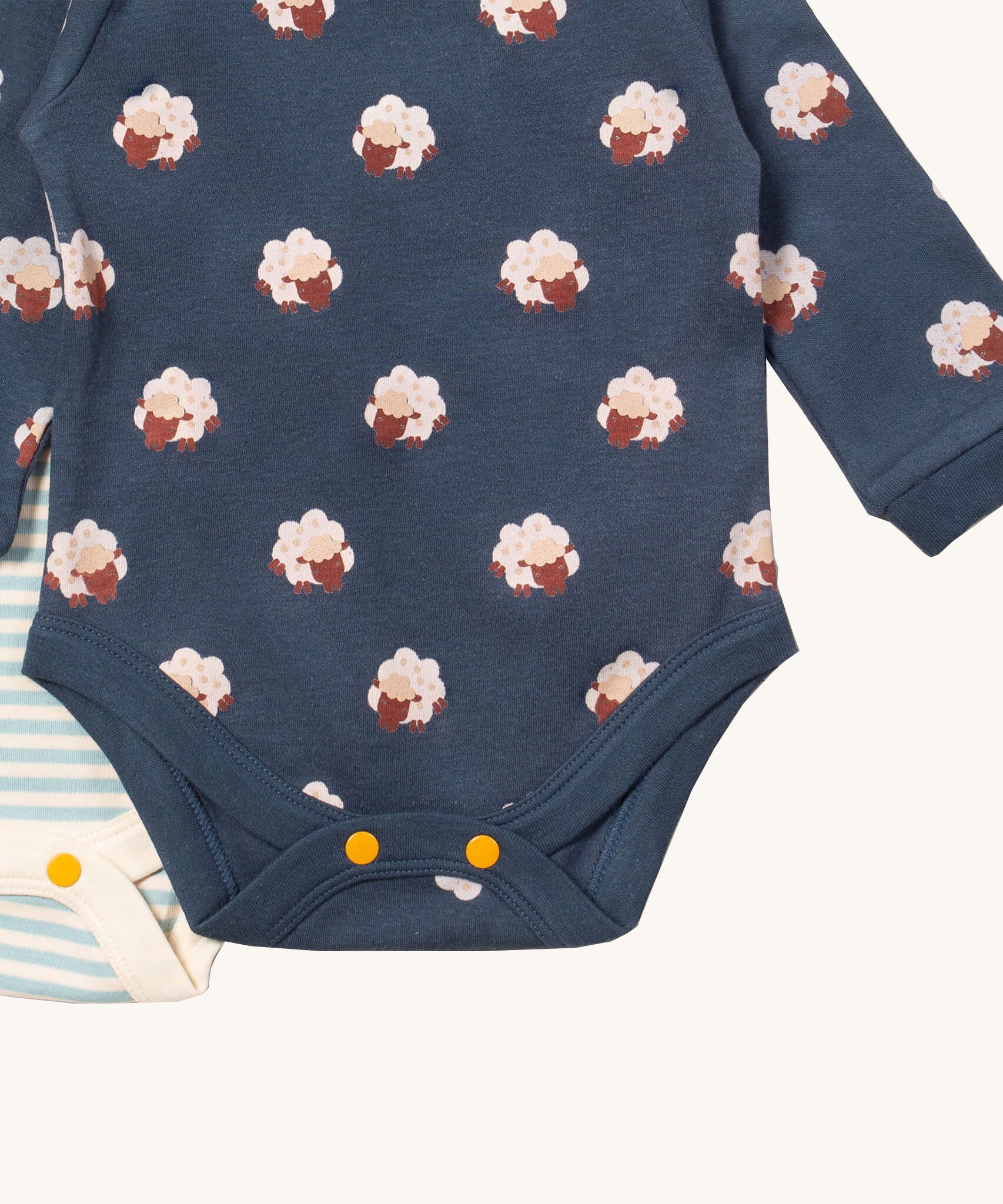 A close up of the sheep Little Green Radicals baby body suit on top of the light blue and cream striped bodysuit showing yellow popper detail around the crotch and leg hole detail on soft organic cotton fabric