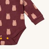 A close up of the brown bear Little Green Radicals baby body suit showing the green and cream stripe detail and yellow popper detail around the crotch on soft dark maroon organic cotton fabric