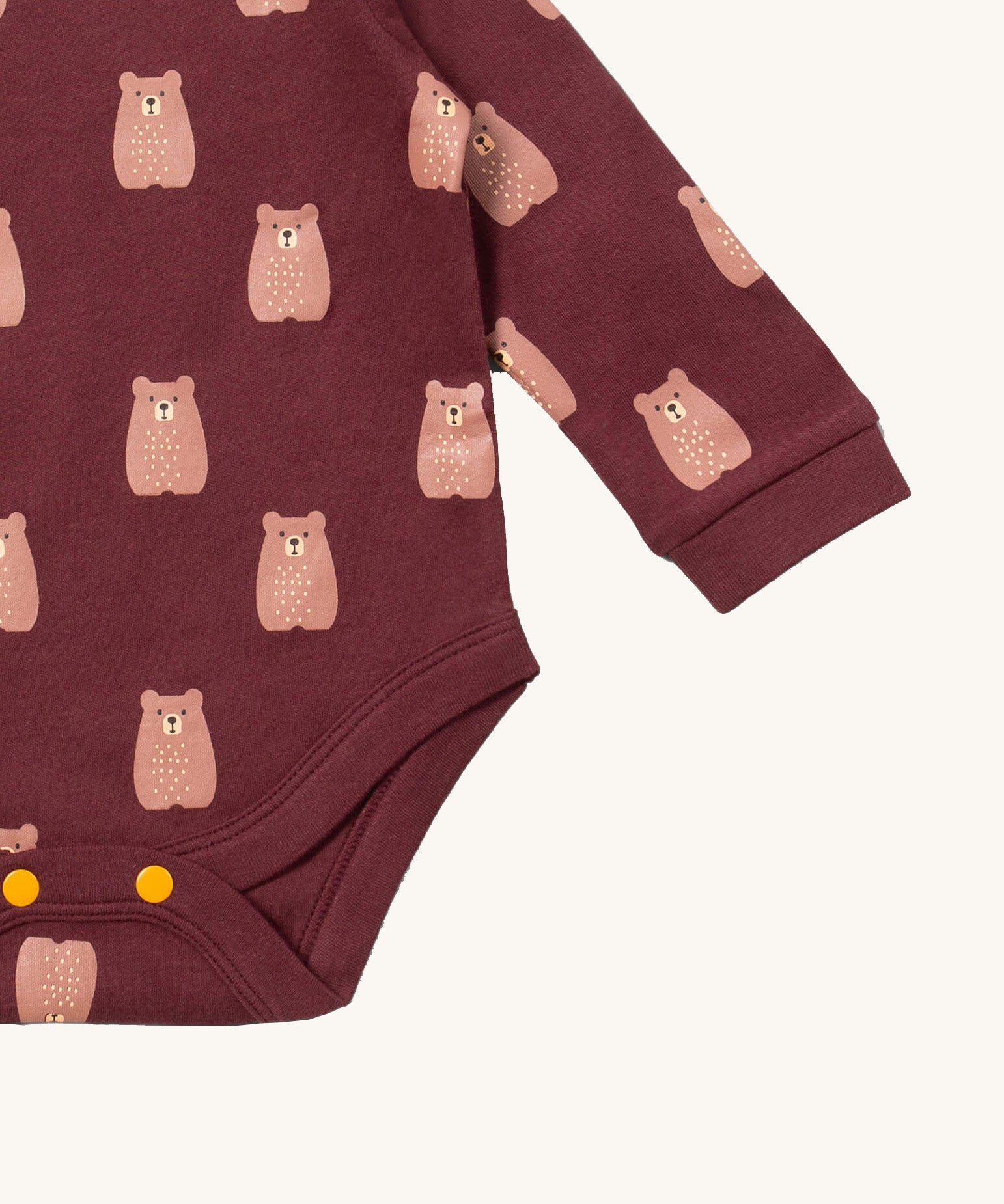 A close up of the brown bear Little Green Radicals baby body suit showing the green and cream stripe detail and yellow popper detail around the crotch on soft dark maroon organic cotton fabric