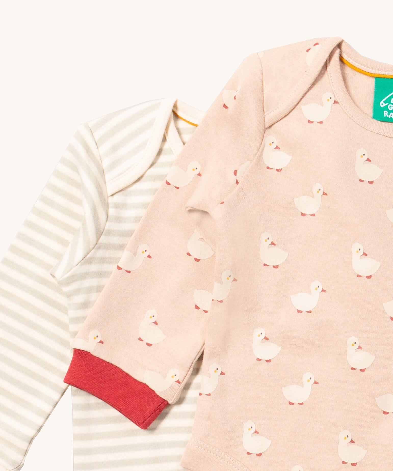 A close up of the duck Little Green Radicals baby body suit on top of the striped bodysuit showing red cuff trim and print detail on soft organic cotton fabric