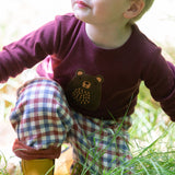 A close up of a child playing in grass and wearing the dark maroon Little Green Radicals teddy bear applique long sleeve t shirt showing the brown bear applique detail.