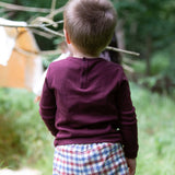 A child standing outside and showing the back of the dark maroon Little Green Radicals teddy bear applique long sleeve t shirt showing the popper fastener detail