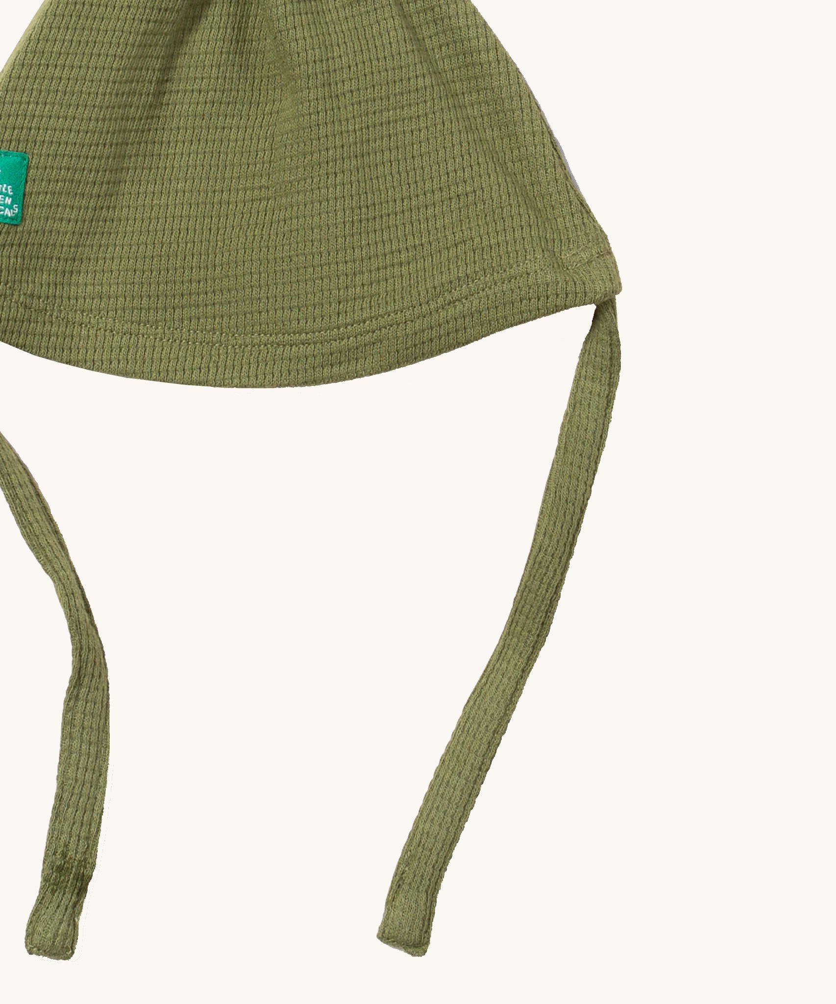 A close up of the Little Green Radicals chive waffle tie hat showing the tie strap for a secure fit and waffle knit detail on green organic cotton fabric