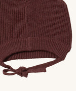 A close up of the Little Green Radicals chocolate knitted beanie hat showing the closed brown tie detail on  organic cotton fabric