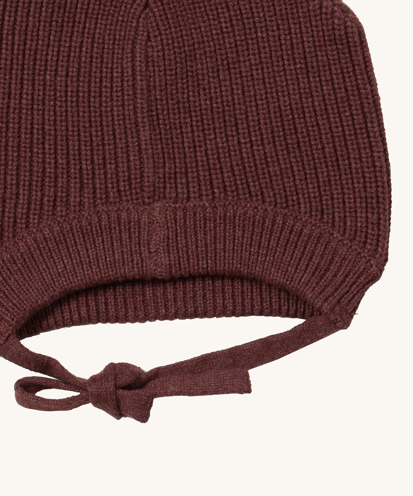 A close up of the Little Green Radicals chocolate knitted beanie hat showing the closed brown tie detail on  organic cotton fabric