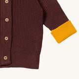 A close up of the Little Green Radicals knitted cardigan in chocolate showing the button detail and a close up of the yellow cuff and hem detail on brown GOTS organic cotton fabric and available at Babipur.