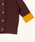 A close up of the Little Green Radicals knitted cardigan in chocolate showing the button detail and a close up of the yellow cuff and hem detail on brown GOTS organic cotton fabric and available at Babipur.