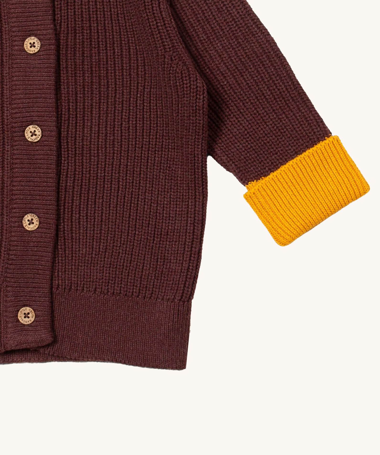 A close up of the Little Green Radicals knitted cardigan in chocolate showing the button detail and a close up of the yellow cuff and hem detail on brown GOTS organic cotton fabric and available at Babipur.