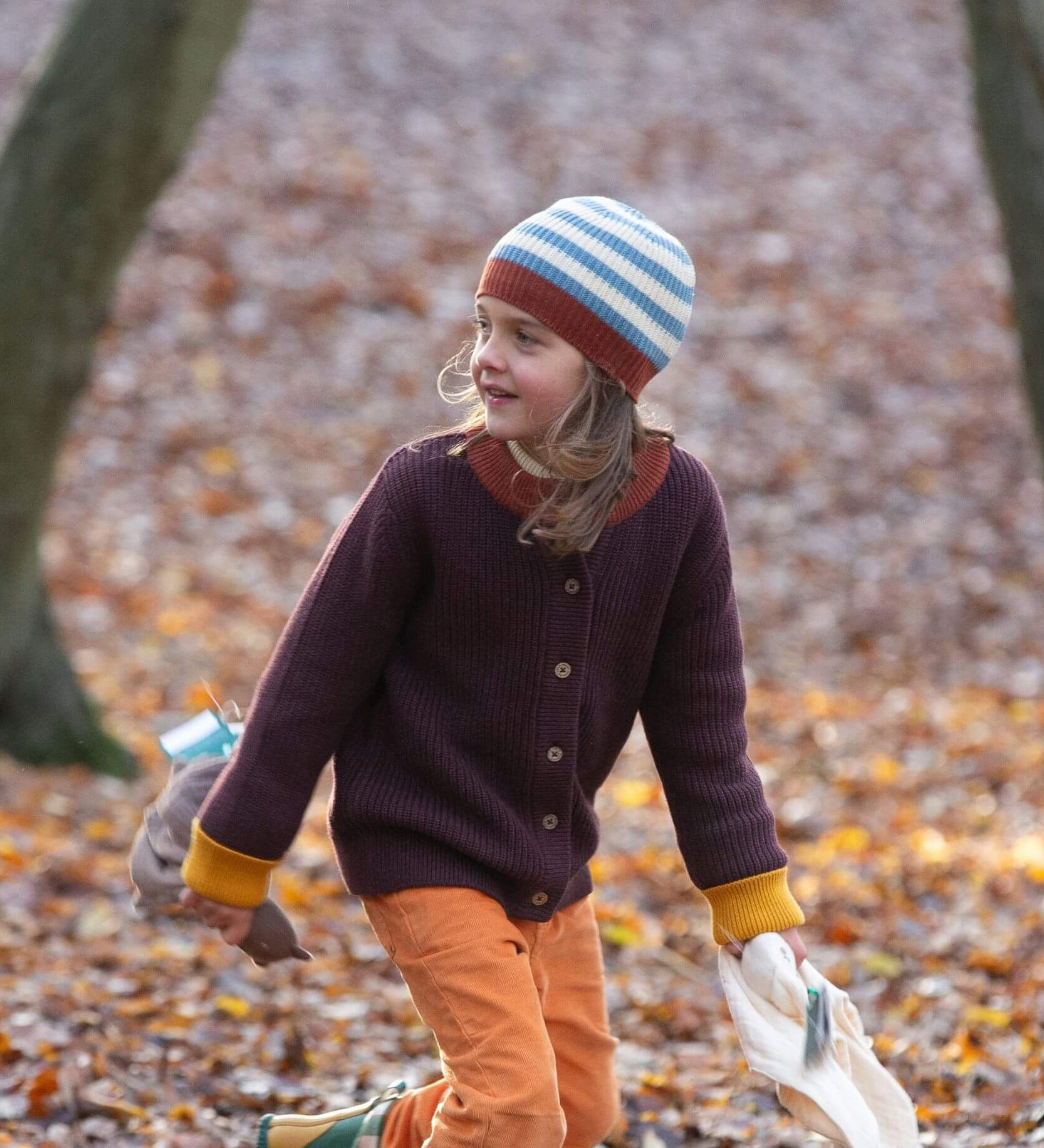 A child wearing the Little Green Radicals knitted cardigan in chocolate outside showing the length and fit of the cardigan 