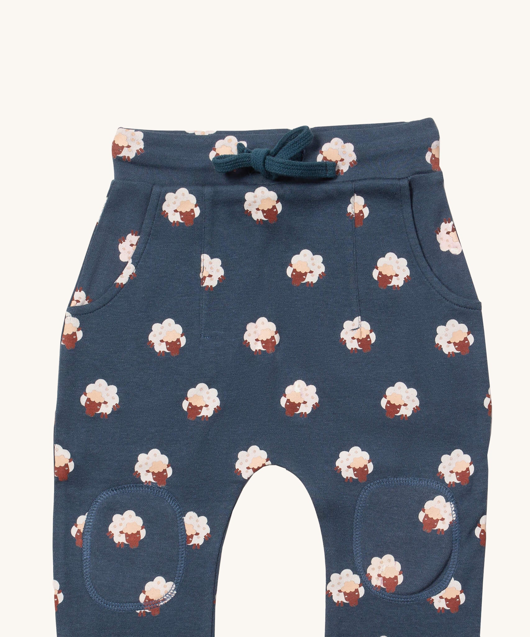 A close up of the Little Green Radicals comfy joggers in sleeping sheep showing the pocket, drawstring and kneepatch detail on navy organic cotton fabric