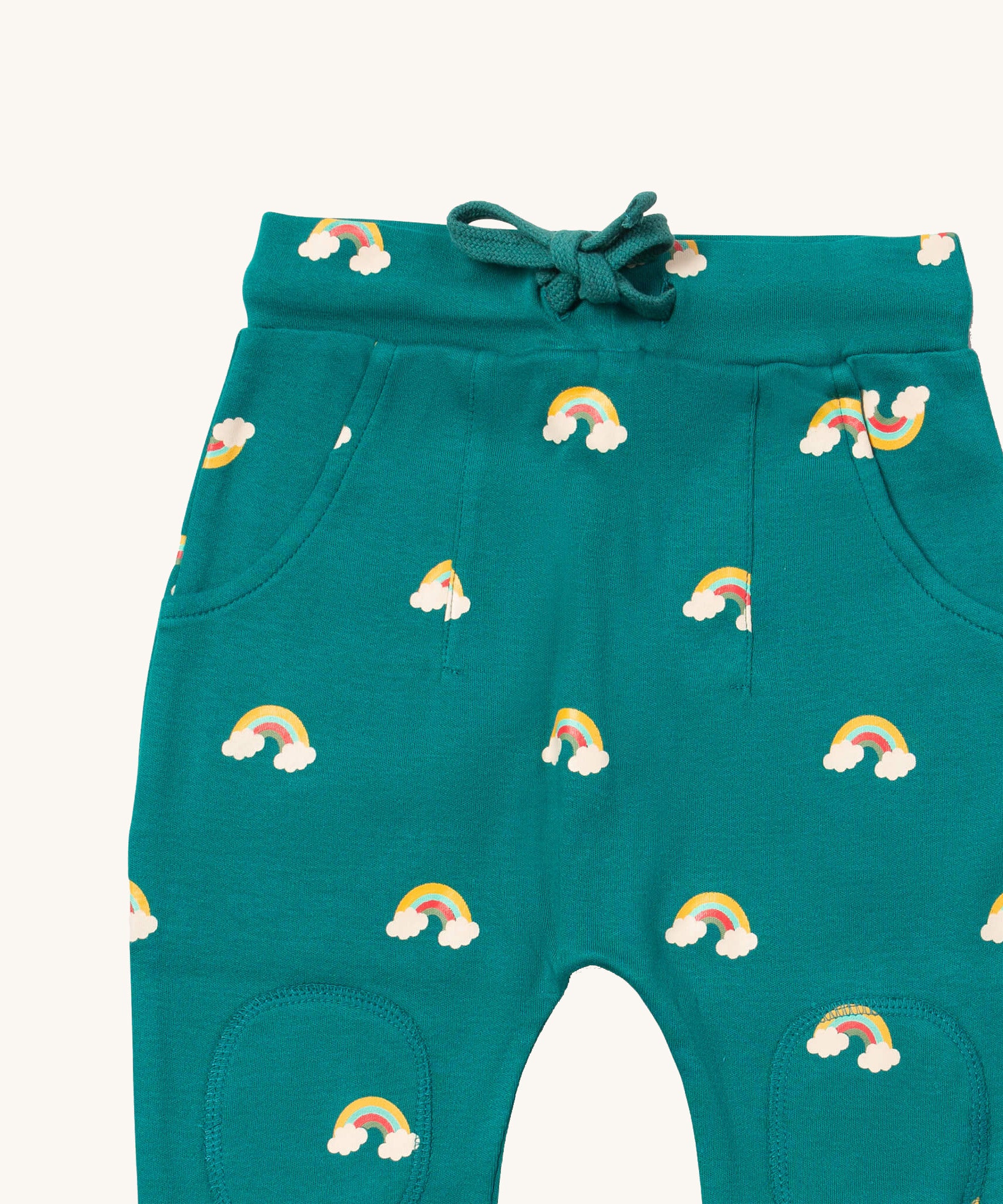 A close up  the Little Green Radicals turquoise rainbow joggers showing the turquoise drawstring, 2 side pockets and stitched on knee patches  on organic cotton fabric.