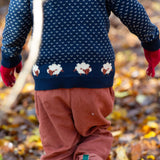 A child walking through leaves in a woodland  and wearing the Little Green Radicals comfy corduroy trousers in ginger with the navy sheep knitted jumper.  A corduroy loose fitted trousers in dark orange organic cotton fabric