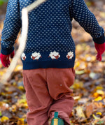 A child walking through leaves in a woodland  and wearing the Little Green Radicals comfy corduroy trousers in ginger with the navy sheep knitted jumper.  A corduroy loose fitted trousers in dark orange organic cotton fabric