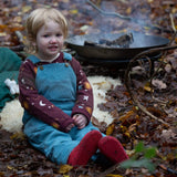 A child sitting down surrounded by leaves and wearing the Little Green Radicals pale blue lined corduroy dungarees