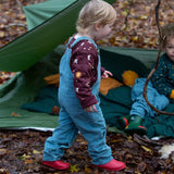 A child walking in the woods and wearing the Little Green Radicals pale blue lined corduory dungarees over the quilted flying birds sweater.
