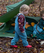 A child walking in the woods and wearing the Little Green Radicals pale blue lined corduory dungarees over the quilted flying birds sweater.