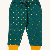 Little Green Radicals cosy joggers in golden stars available at Babipur.. A soft GOTS organic cotton dark turquoise jogger pants with yellow stars and matching yellow trim. Features 2 side pockets a matching turquoise waist drawstring and knee patches.