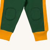 A close up  the Little Green Radicals golden stars cosy joggers showing the stitched on knee patches and yellow cuff trim on soft green organic cotton fabric
