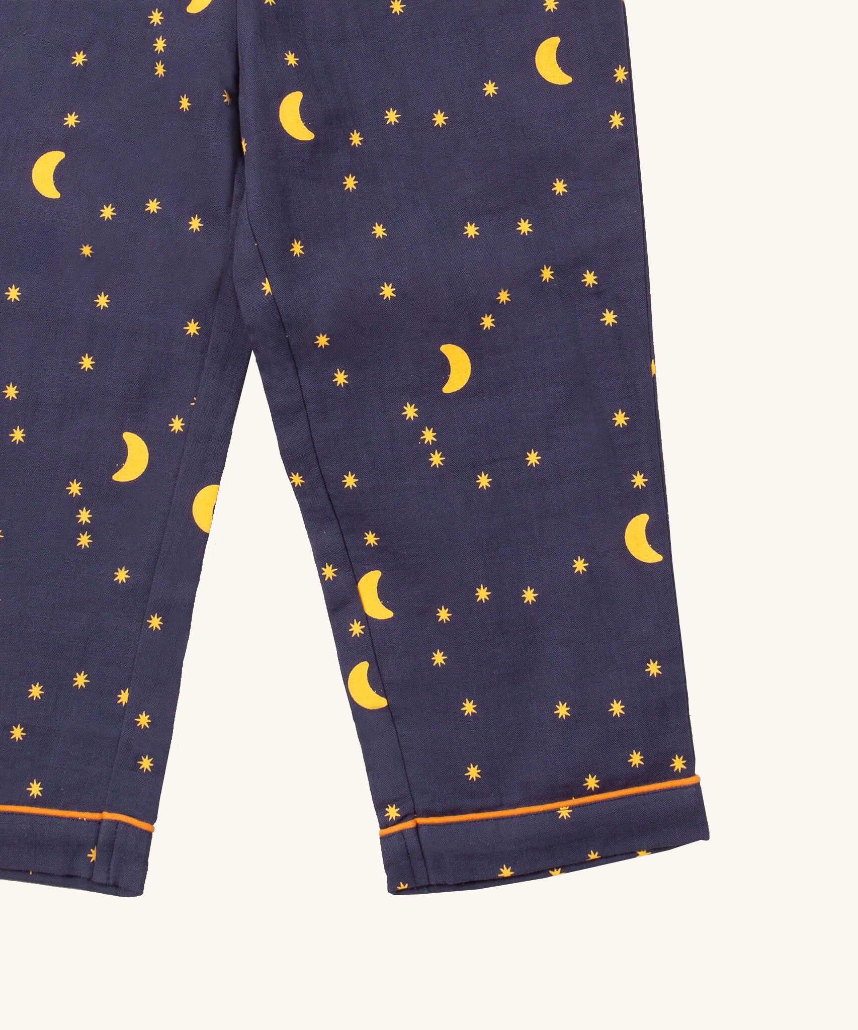A close up of the Little Green Radicals classic pyjama bottoms from the dark night classic set. Showing the yellow trim around the bottom of the legs and a close up of the starry night print on navy organic cotton fabric.