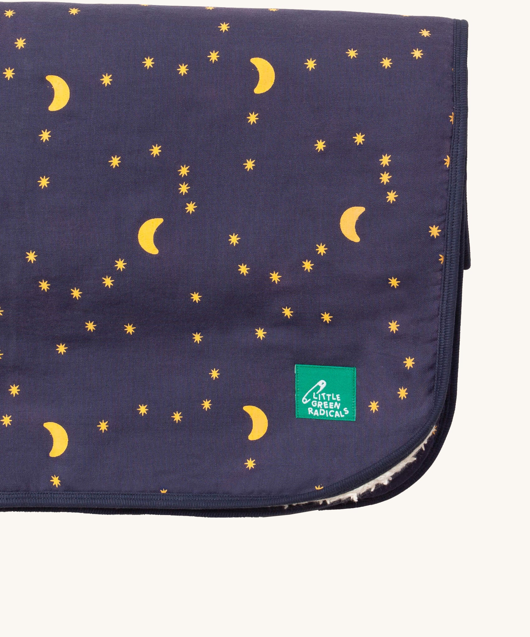A close up of the Little Green Radicals dark night sherpa hooded blanket. Showing the brand patch detail stitched on the corner on navy soft organic cotton fabric