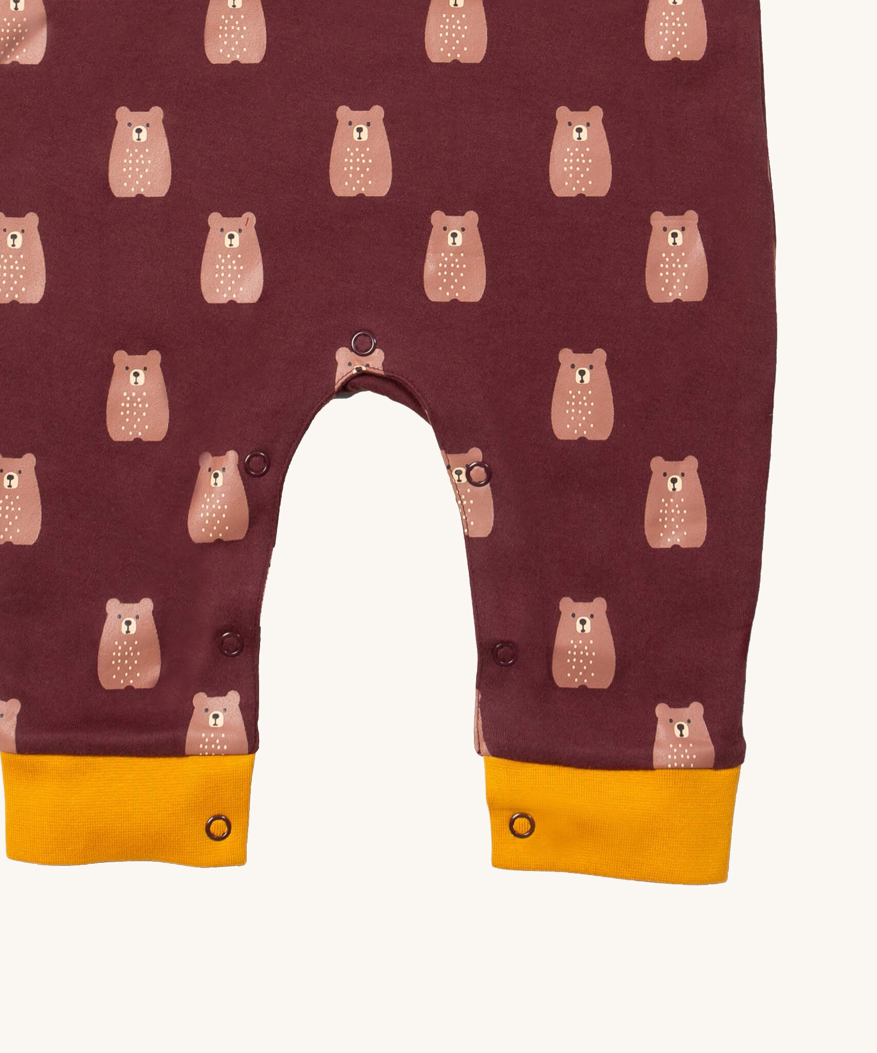 A close up of the Little Green Radicals everyday dungarees in brown bears showing the popper fastener detail around the crotch and yellow trim detail on the leg cuff on dark maroon organic cotton fabric.