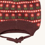 A close up of the Little Green Radicals flower collecting knitted beanie hat showing the closed dark orange tie detail on brown organic cotton fabric