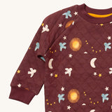 A close up of the Little Green Radicals flying birds quilted sweatshirt that's available at Babipur. Showing the collar and cuff detail dark maroon organic cotton fabric with cute prints of flying birds